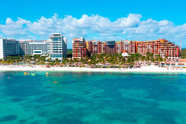 Beachfront resort buildings with white sand beach and turquoise water with boats