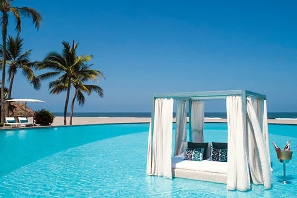 Luxury resort pool with cabana, palm trees, and ocean view under clear blue sky